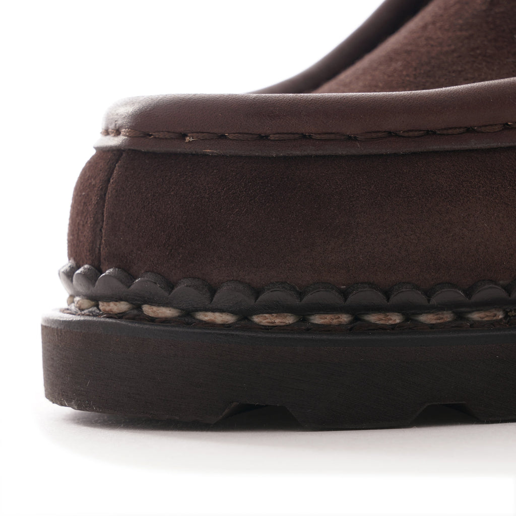 Close-up of the stitching and sole detail of a brown suede shoe.