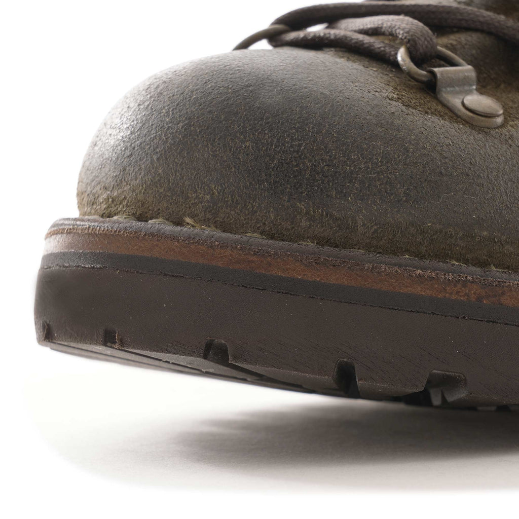 A close-up of the front toe area and thick sole of a dark olive-green hiking boot.