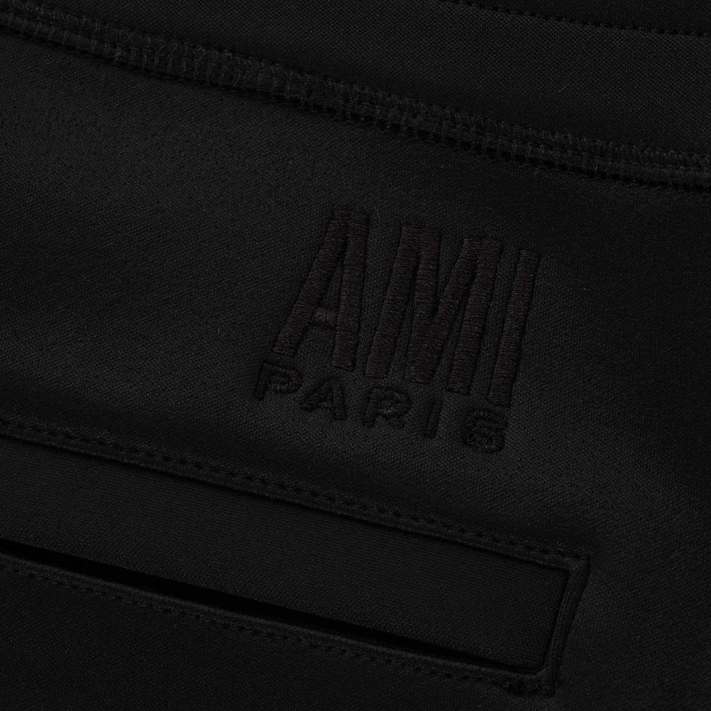Detail of the AMI Paris logo embroidered into the black jogging bottoms' fabric.