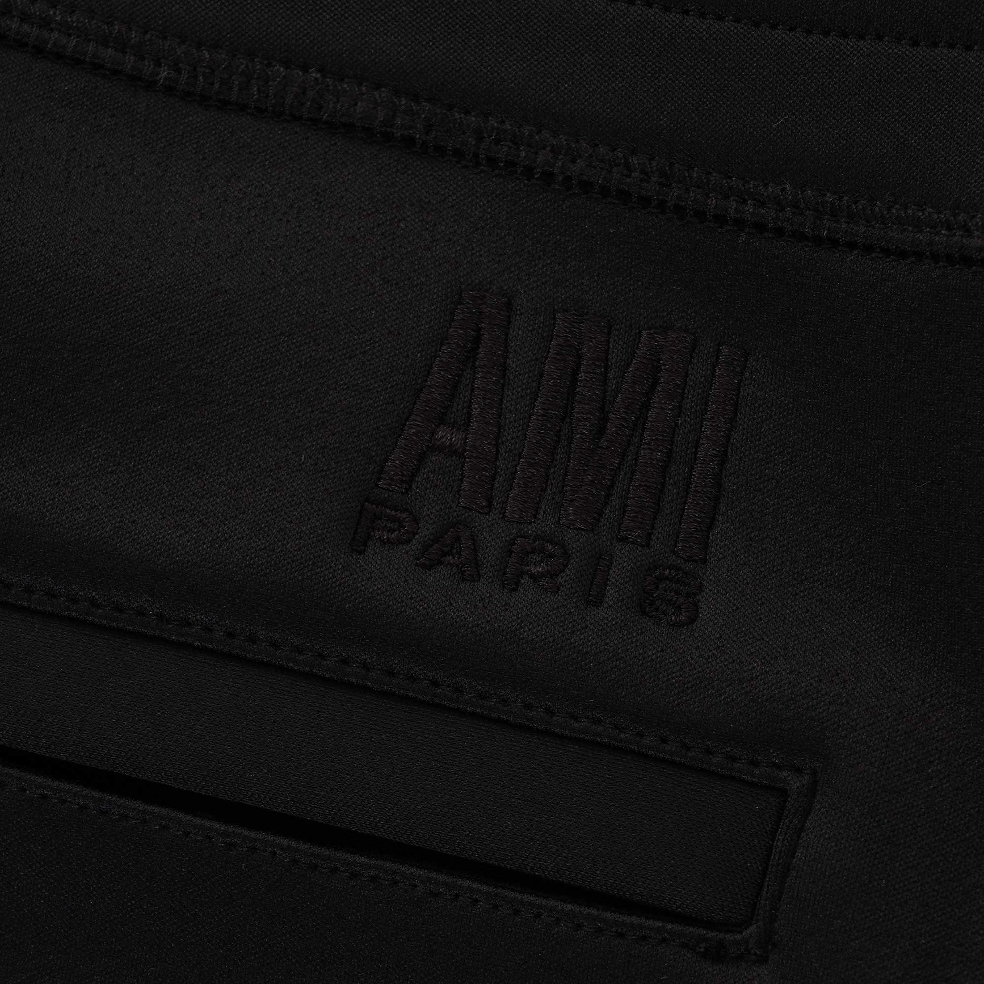 Detail of the AMI Paris logo embroidered into the black jogging bottoms' fabric.