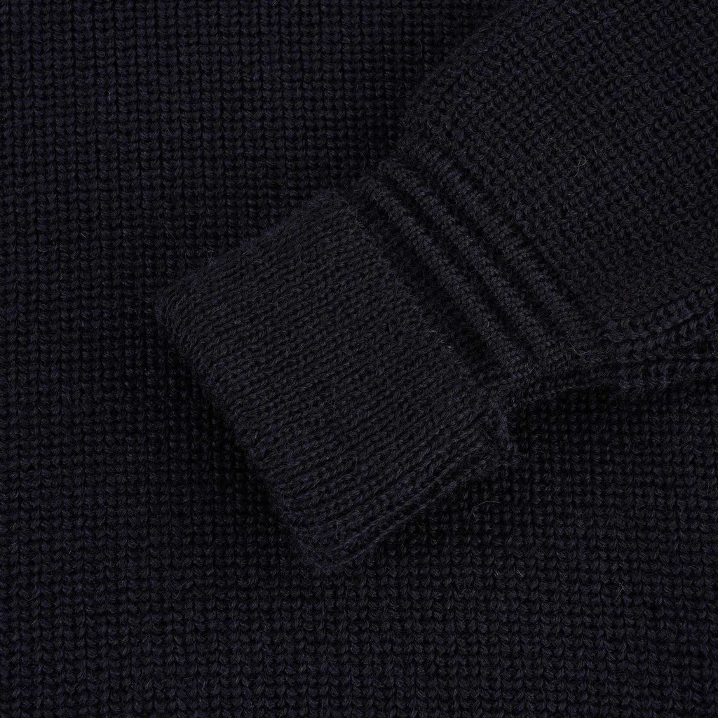 Close-up of the ribbed cuff of a navy blue jumper sleeve.