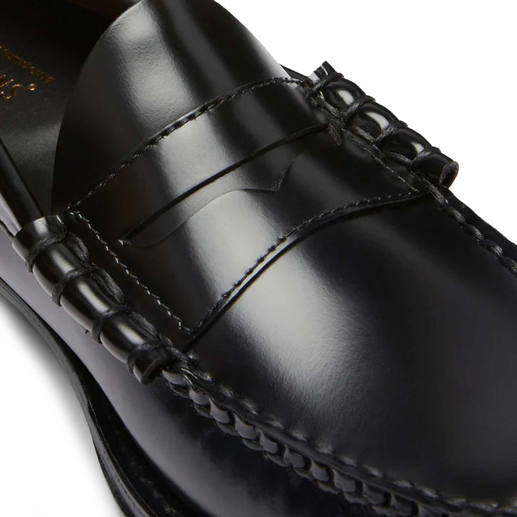 A close-up view of the front of a black leather Penny Loafer shoe.